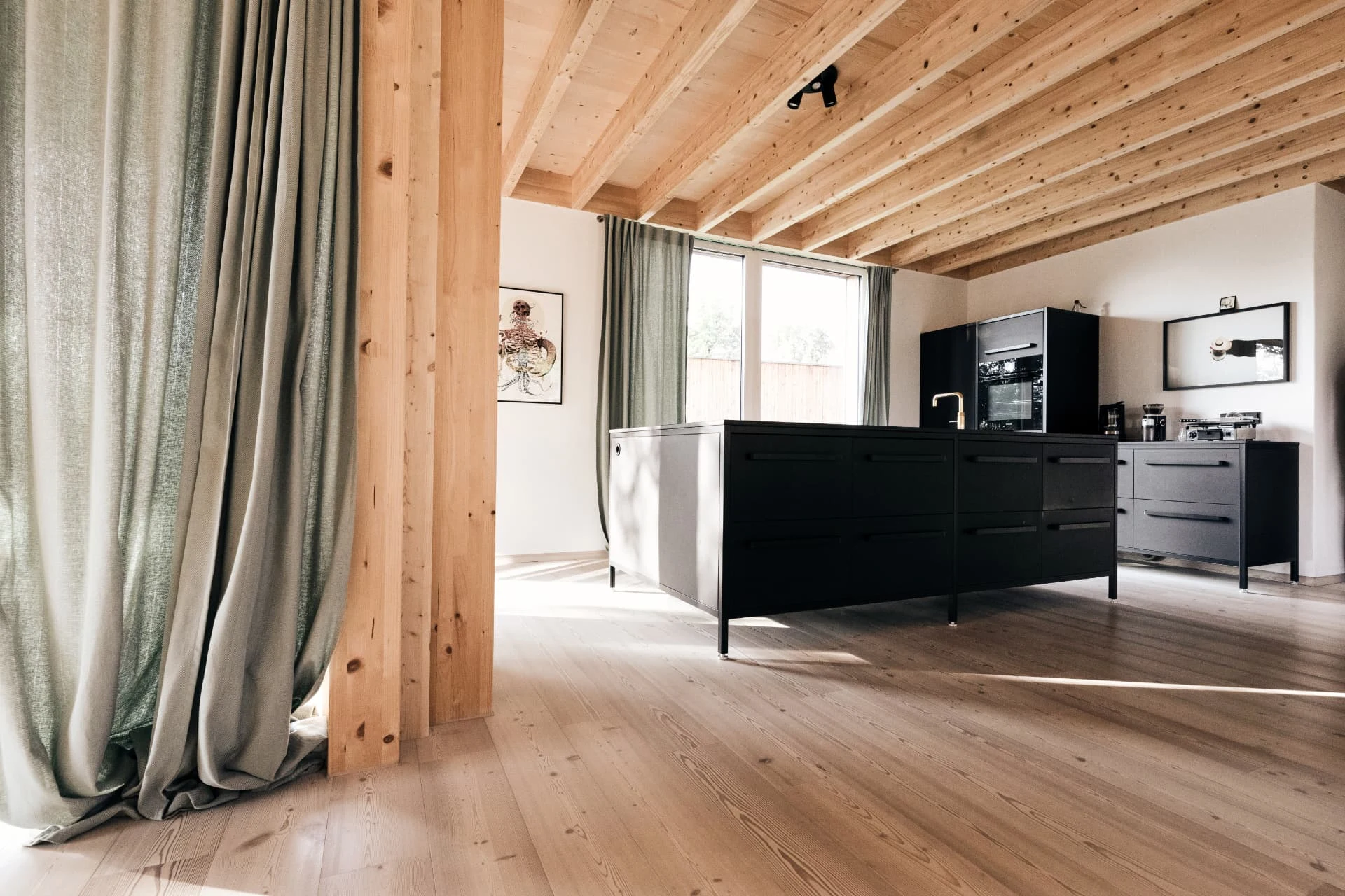 Schwarze Modulküche in hellem Holzhaus mit Deckenbalken und großen Fenstern