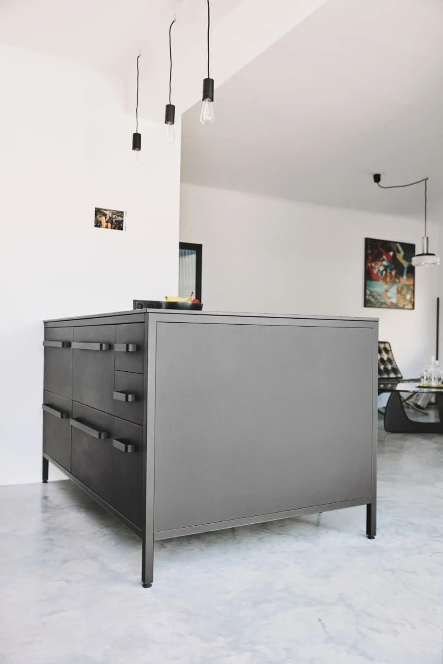 Moderne keep Kücheninsel in Grau mit schwarzen Metallgriffen und hängenden Pendelleuchten vor weißer Wand.