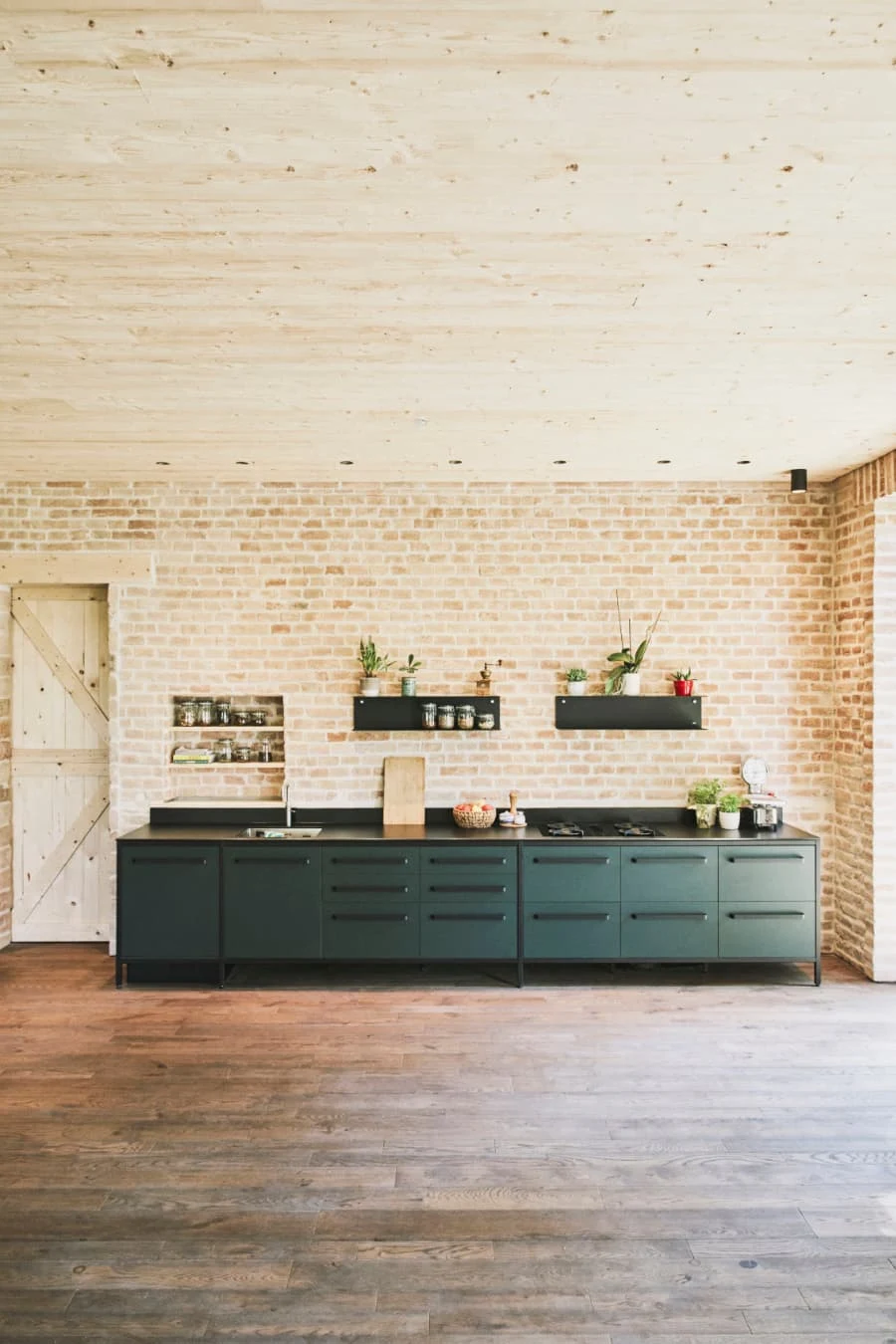 Moderne Modulküche mit dunkelgrünen Fronten und schwarzer Arbeitsplatte vor Ziegelwand in Loft-Raum mit Holzboden.