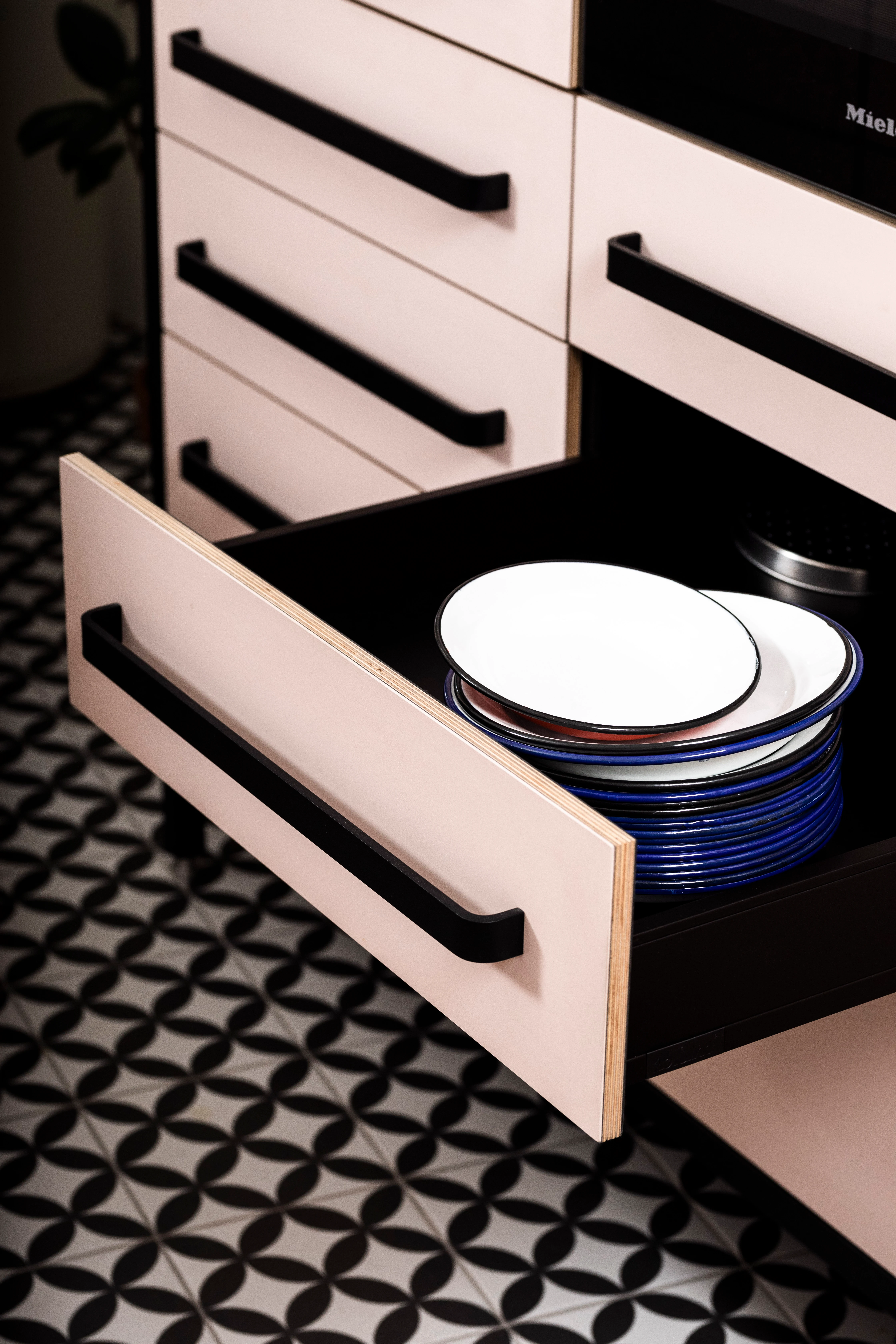Offene Schublade einer kitchen to keep mit rosa Linoleum-Front, schwarzem Griff und gestapeltem Geschirr