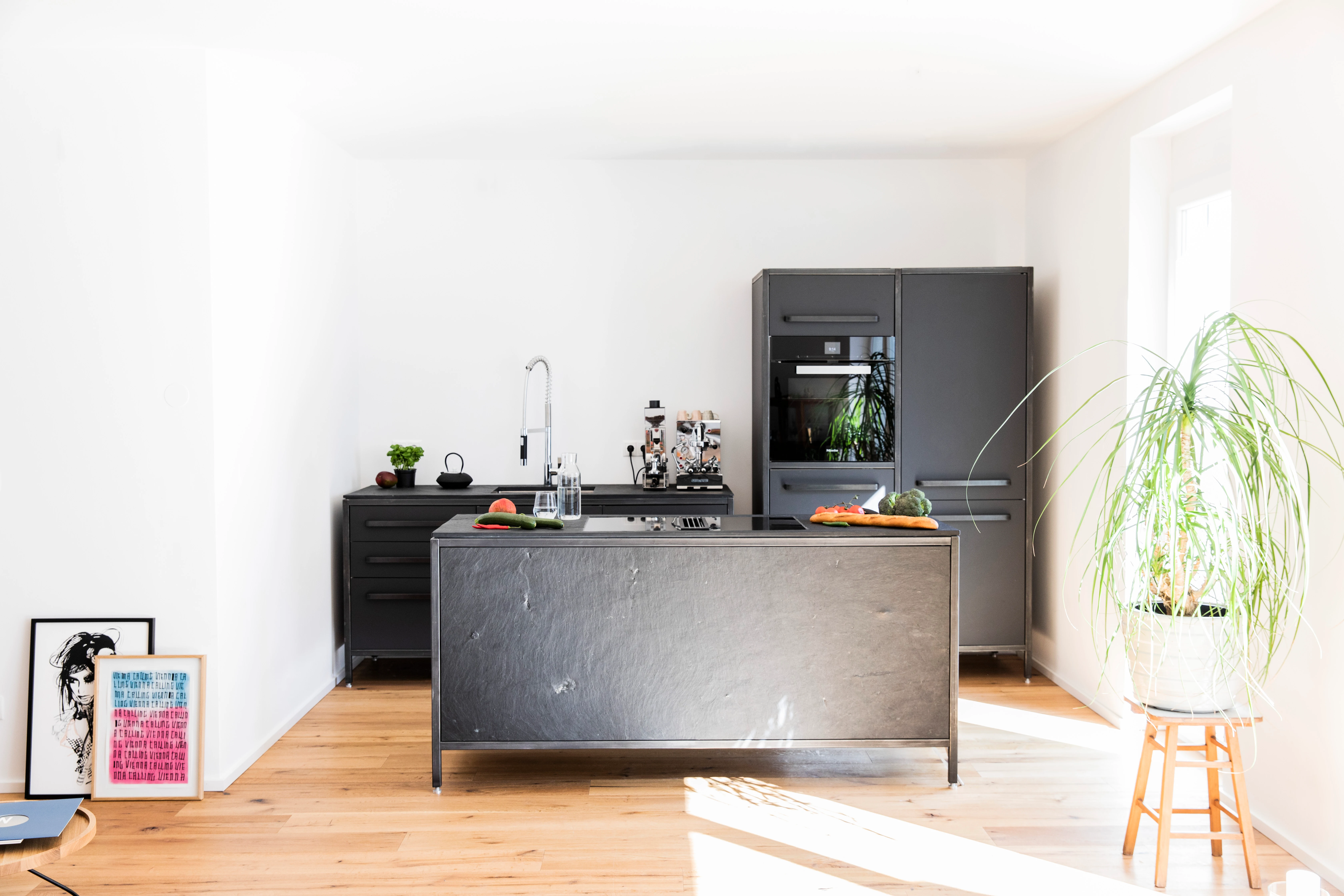 Moderne Küche mit grauer Insel, schwarzen Schränken, Holzboden und Pflanzen