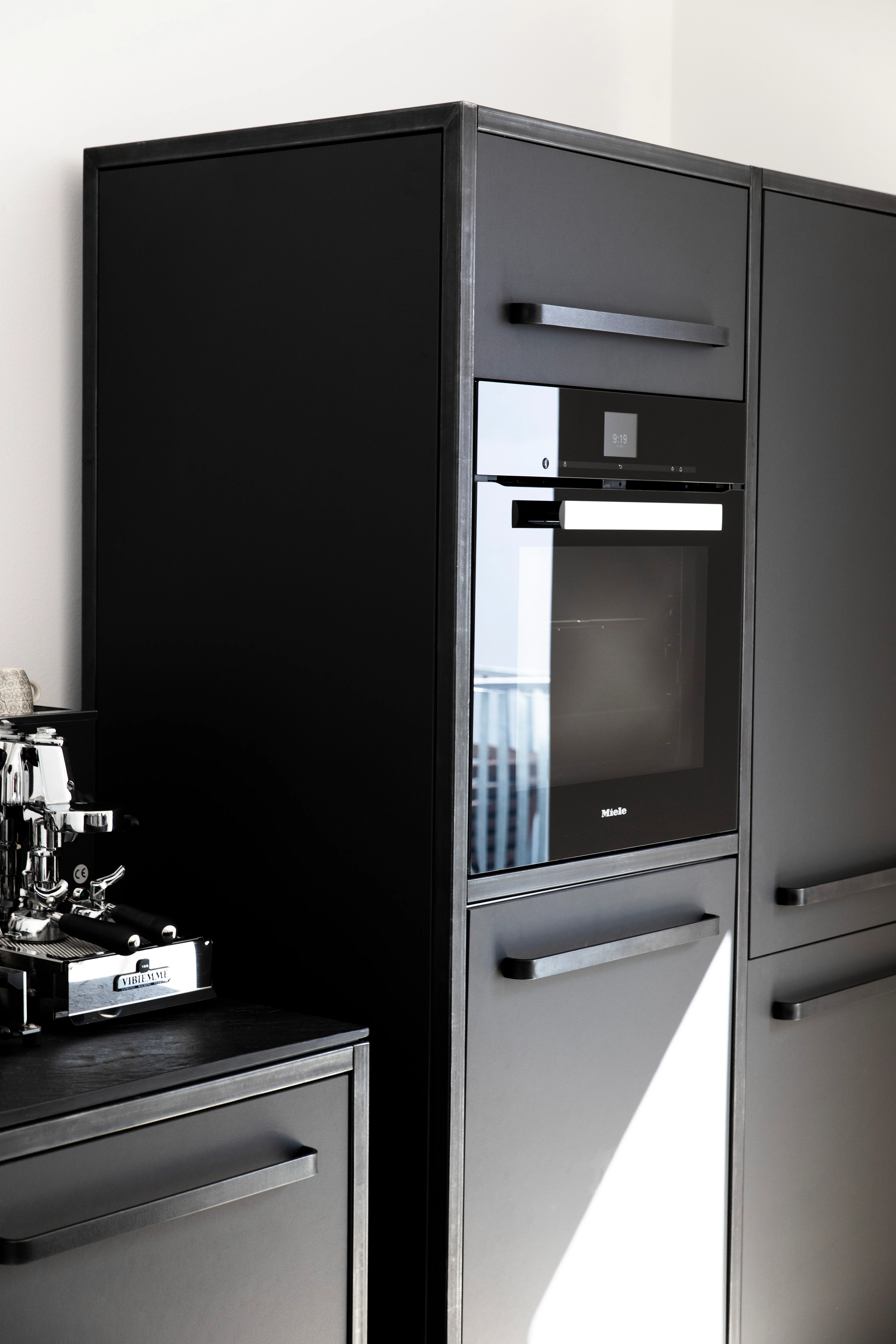 Moderne schwarze Designerküche mit Miele-Einbaugeräten, minimalistisches Design mit schwarzen Griffen und Edelstahl-Akzenten.