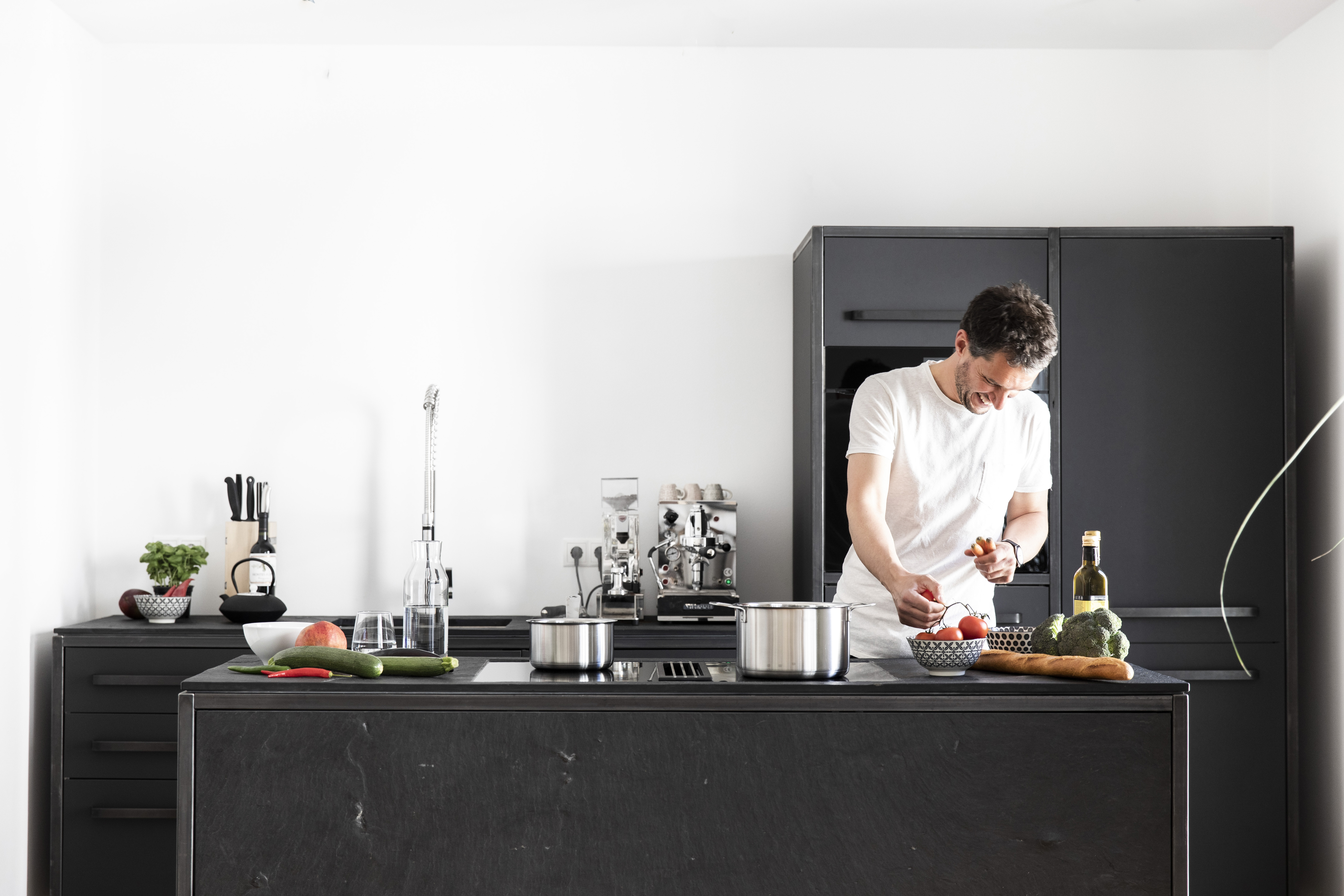 Mann kocht allein an einer schwarzen keep Kücheninsel mit Espressomaschine