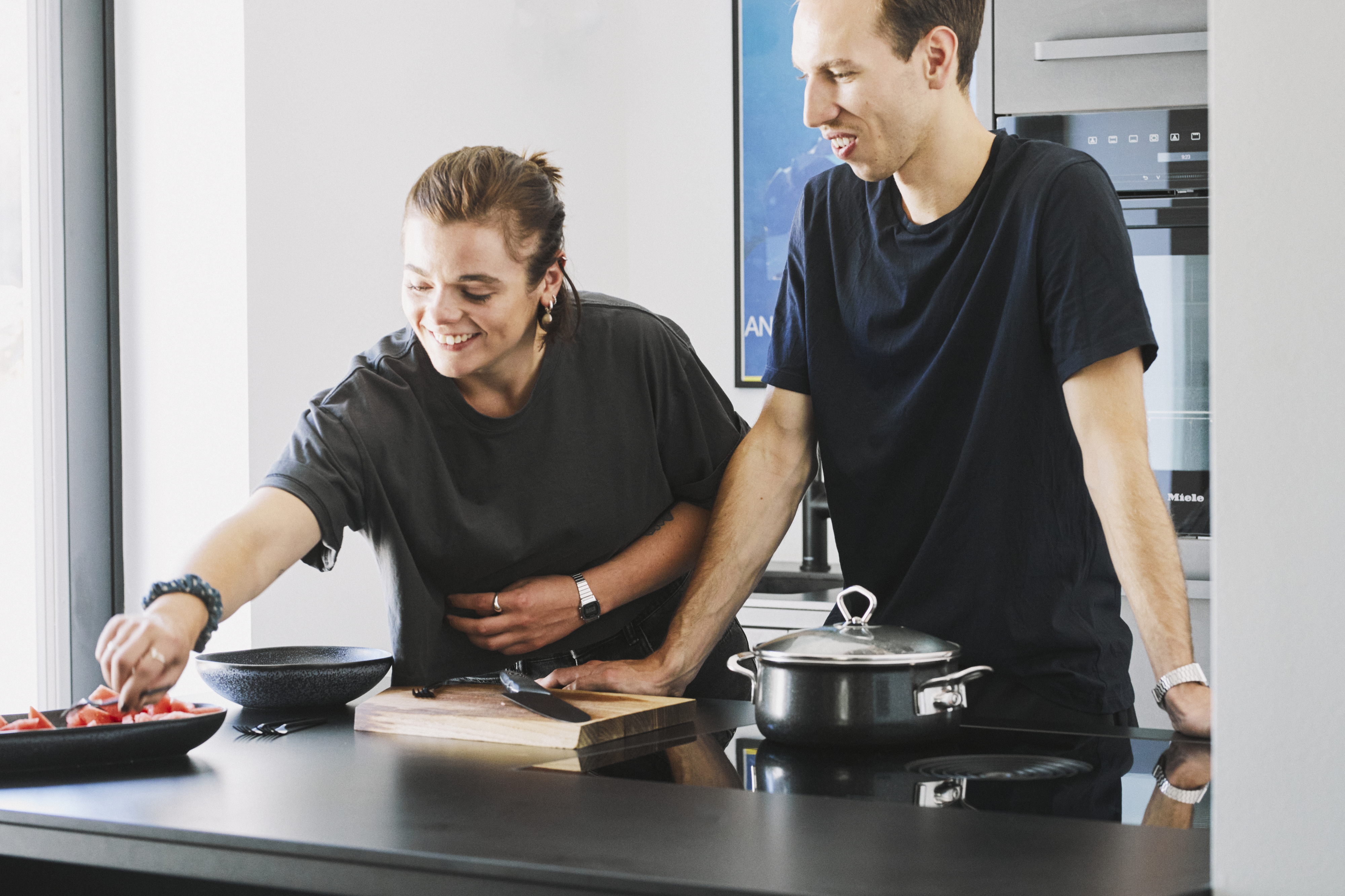 Junges Paar lacht beim Kochen in moderner schwarzer kitchen to keep